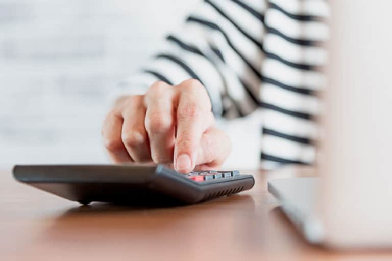 a patients hand using a calculator to determine the cost of her dental implant procedure.